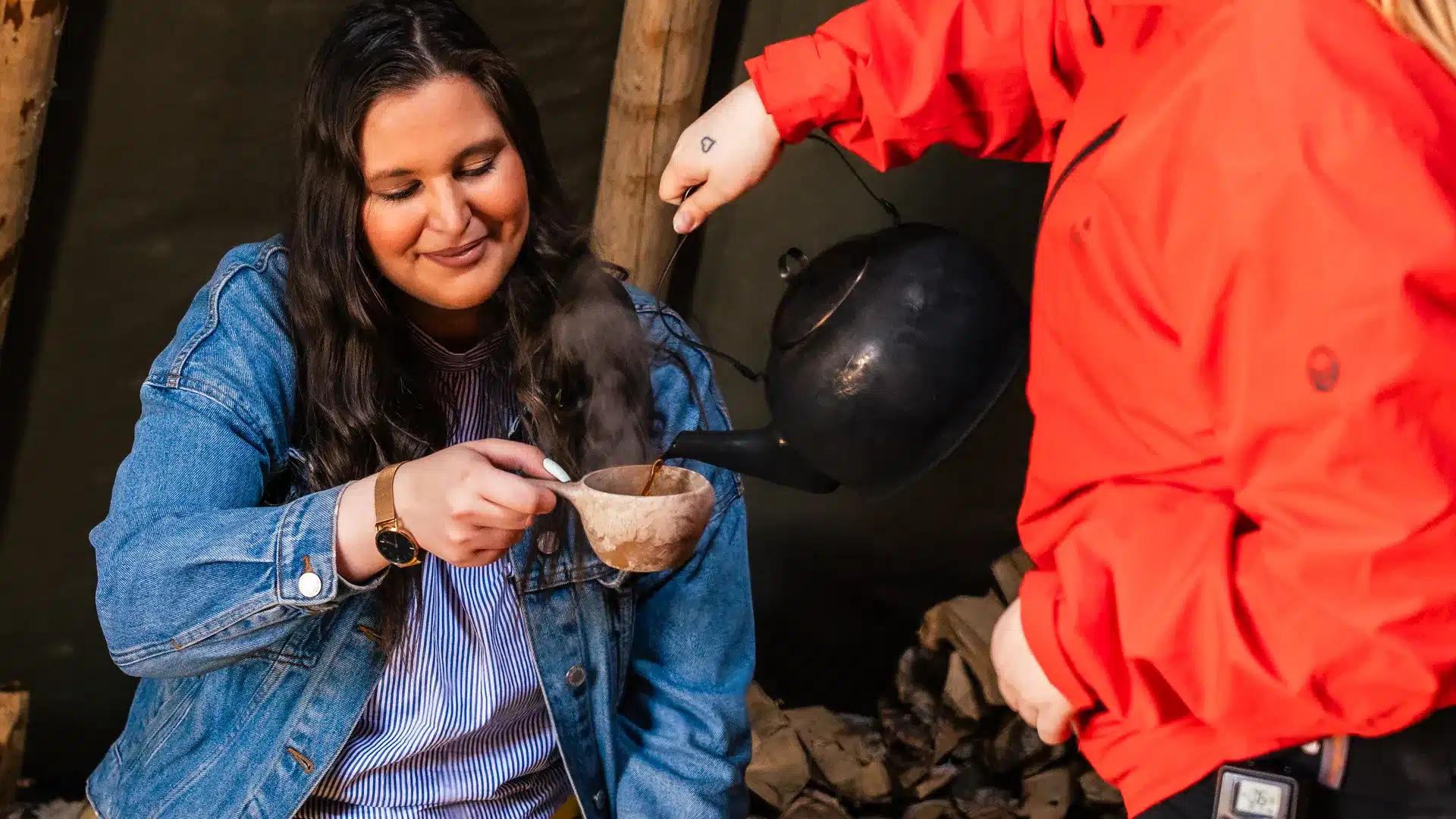 Visitor enjoying coffee by a campfire with a reindeer guide